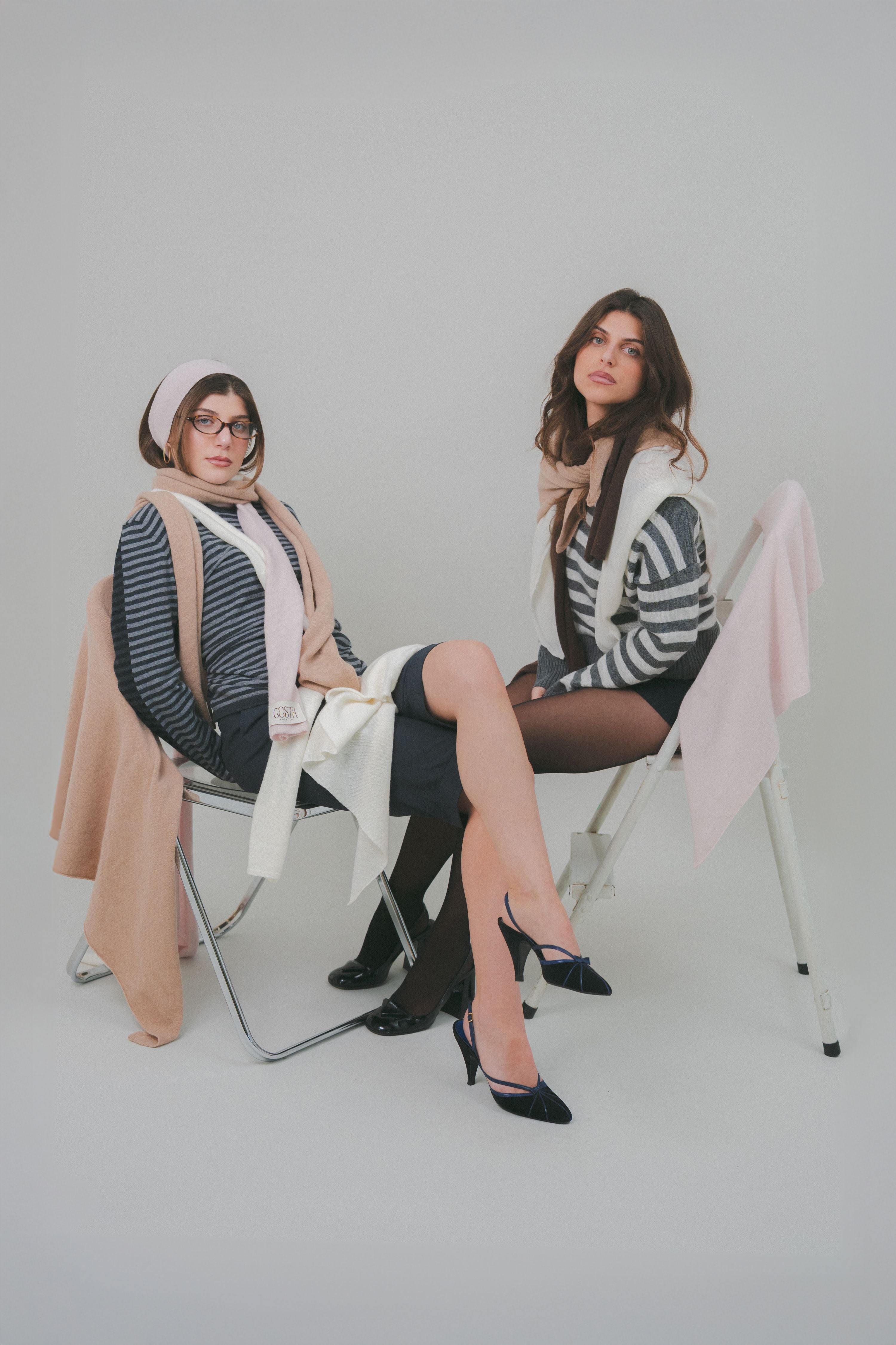 Editorial photography of models showcasing a full knitwear look by Costa Knit Atelier, featuring layered triangle and thin scarves in brown, beige, pink, and white premium cashmere.
