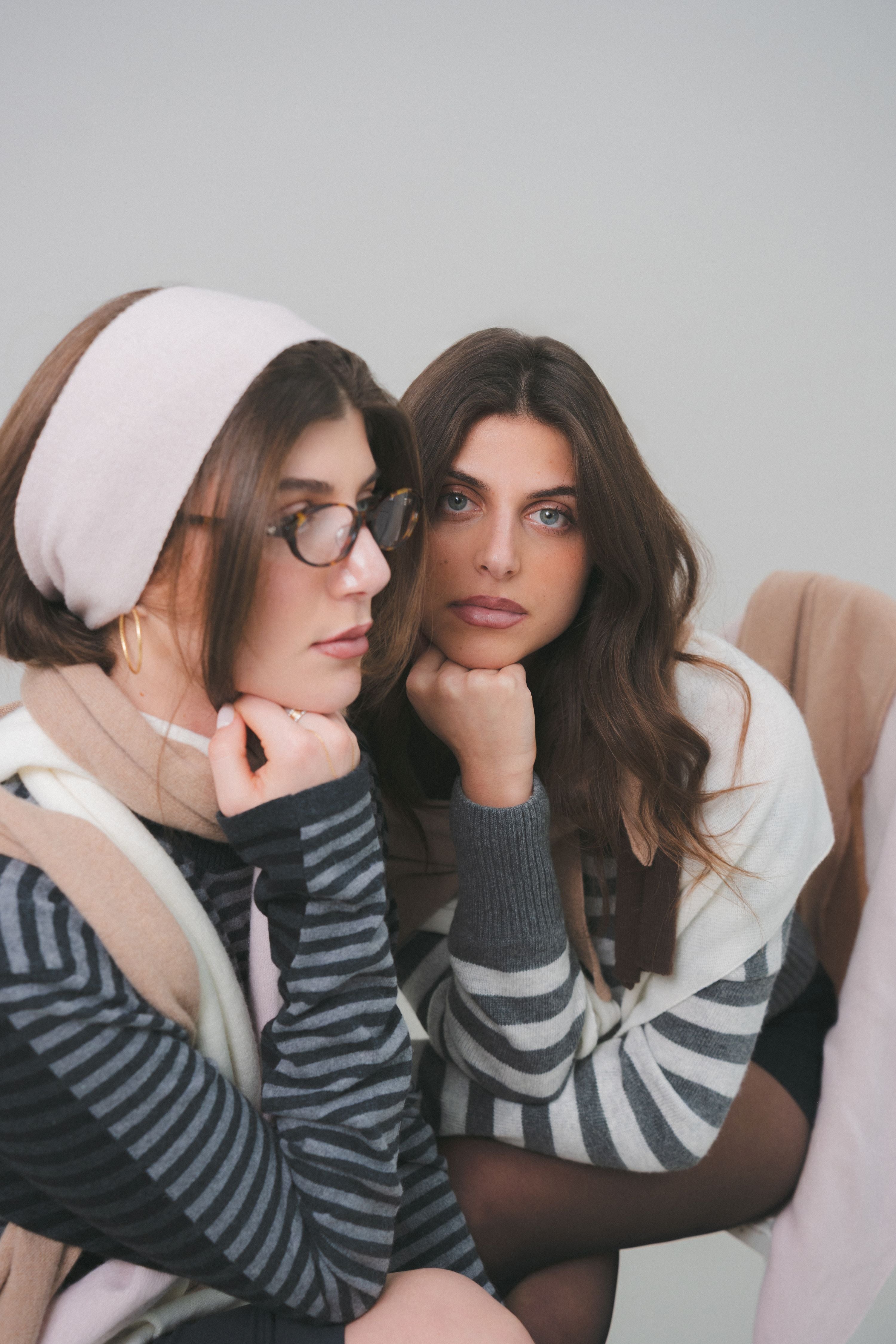 Close-up editorial photography of models wearing a light pink headband and beige cashmere scarf by Costa Knit Atelier, highlighting the soft texture of premium merino wool.