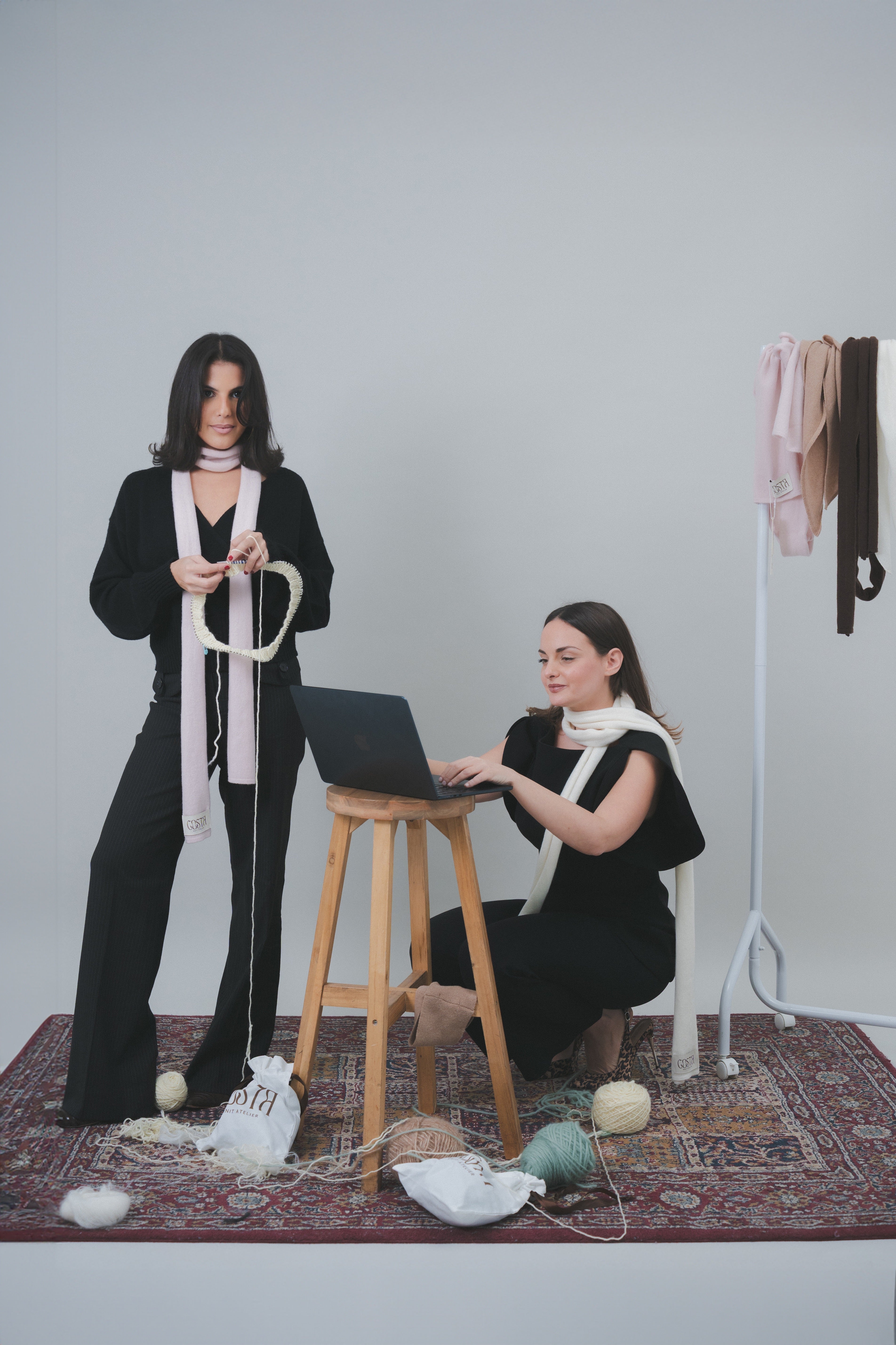 Costa Knit Atelier founders at work, one hand-knitting with premium wool and the other managing the digital atelier, showcasing the blend of traditional craft and modern design.
