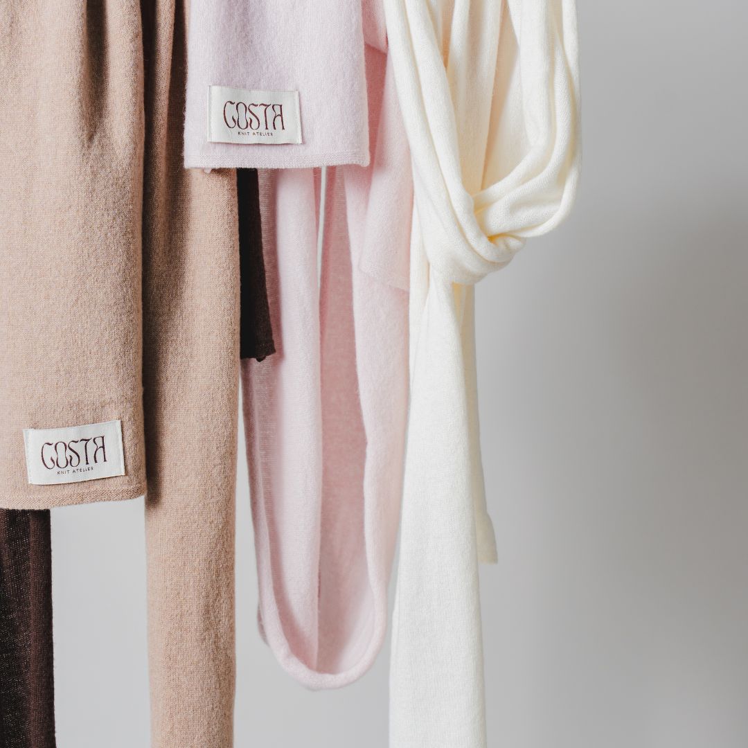 A display of Costa Knit Atelier scarves hanging to showcase their diverse textures and the brand's luxury labels, highlighting the premium quality of our handcrafted knitwear