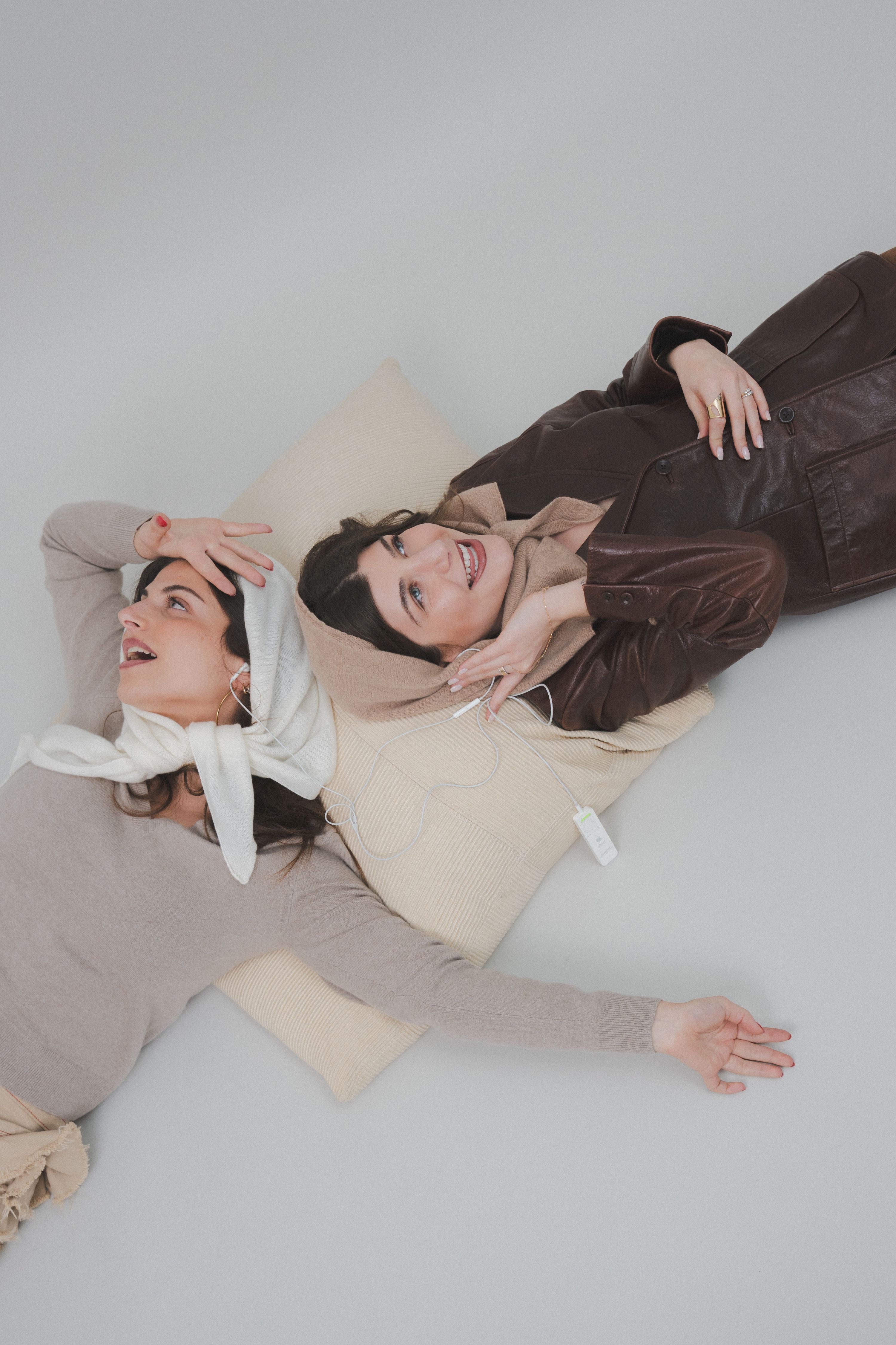 Editorial shot of two models listening to music on headphones and having fun, wearing Costa Knit Atelier headbands and scarves to showcase a contemporary and creative luxury lifestyle.
