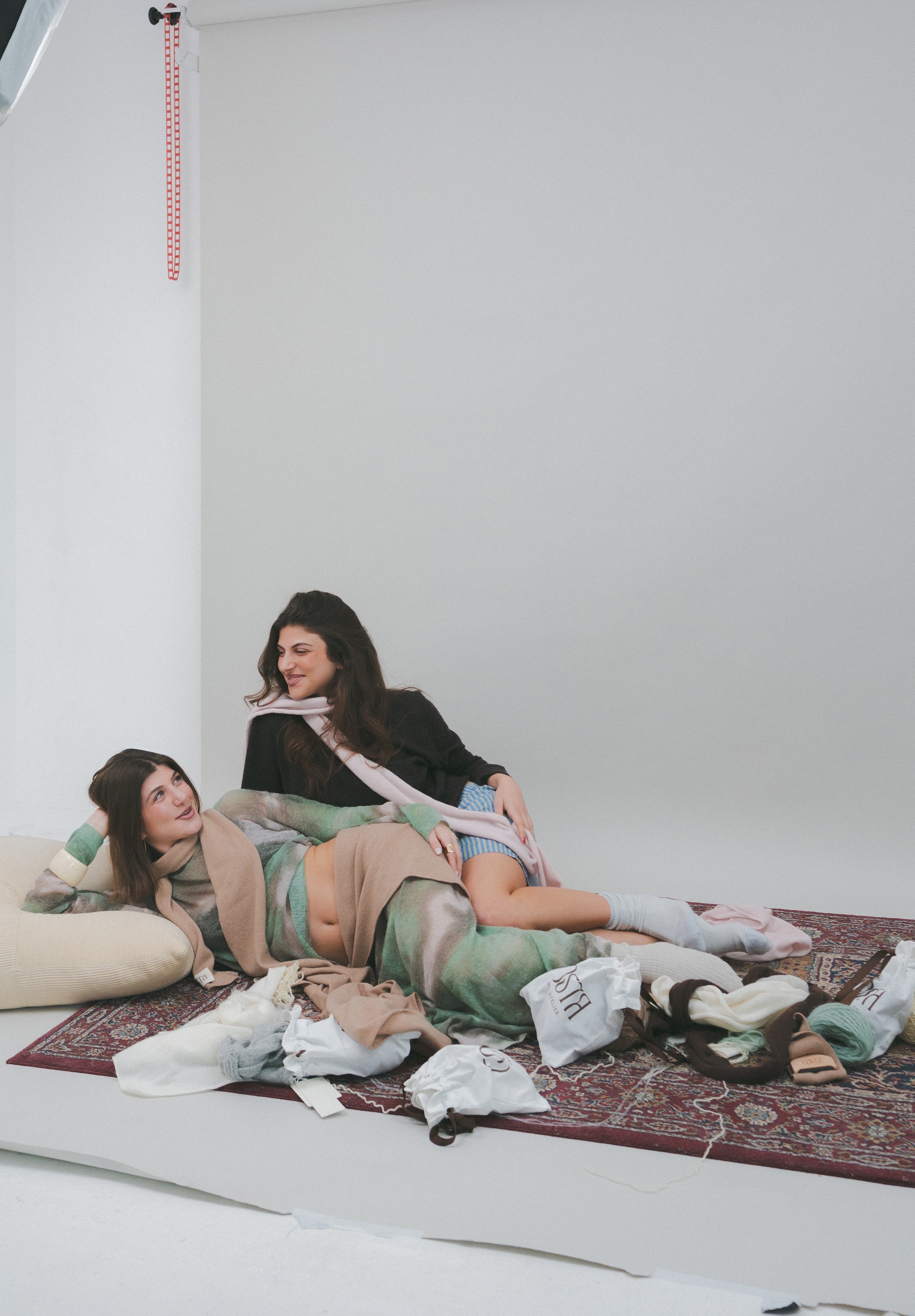 Lifestyle editorial of models on a vintage rug with Costa Knit Atelier accessories, showcasing the soft textures and natural color palette of our luxury knitwear collection