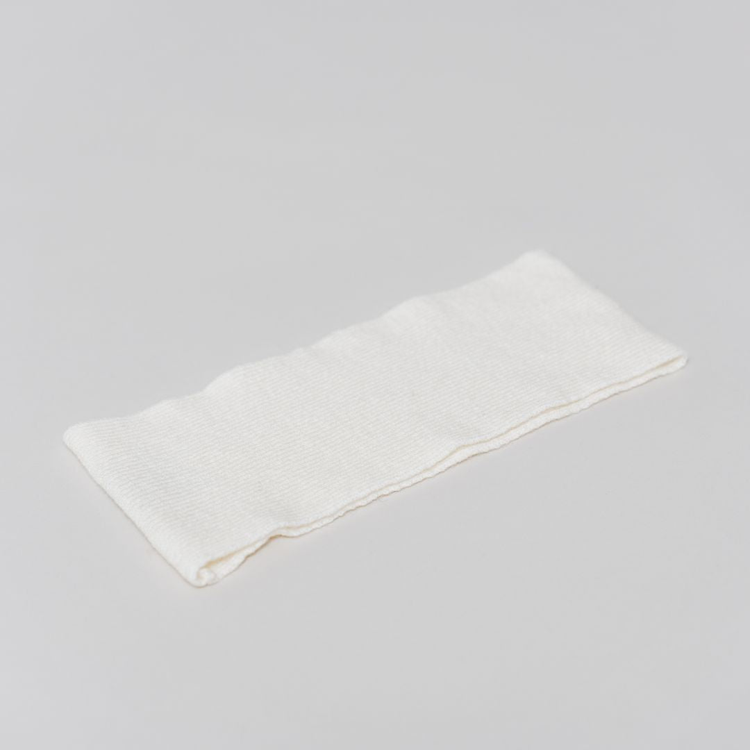 Flat lay of the white Headband by Costa Knit Atelier, handcrafted from a premium cashmere and extra-fine merino wool blend for ultimate comfort.