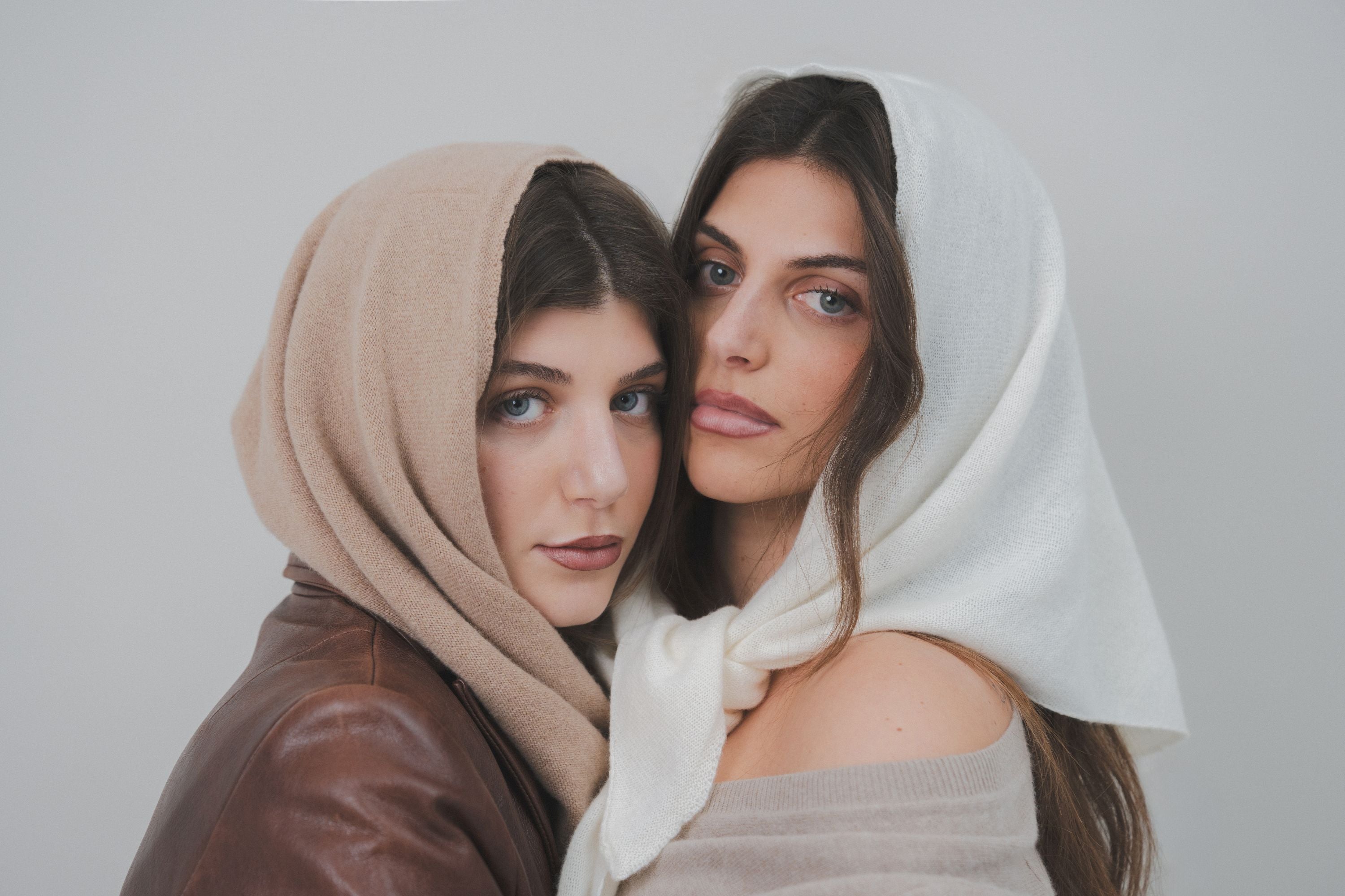 Two models wearing the Costa Knit Atelier Triangle Scarf in white and beige, showcasing the luxury texture of premium cashmere and artisanal Mediterranean style