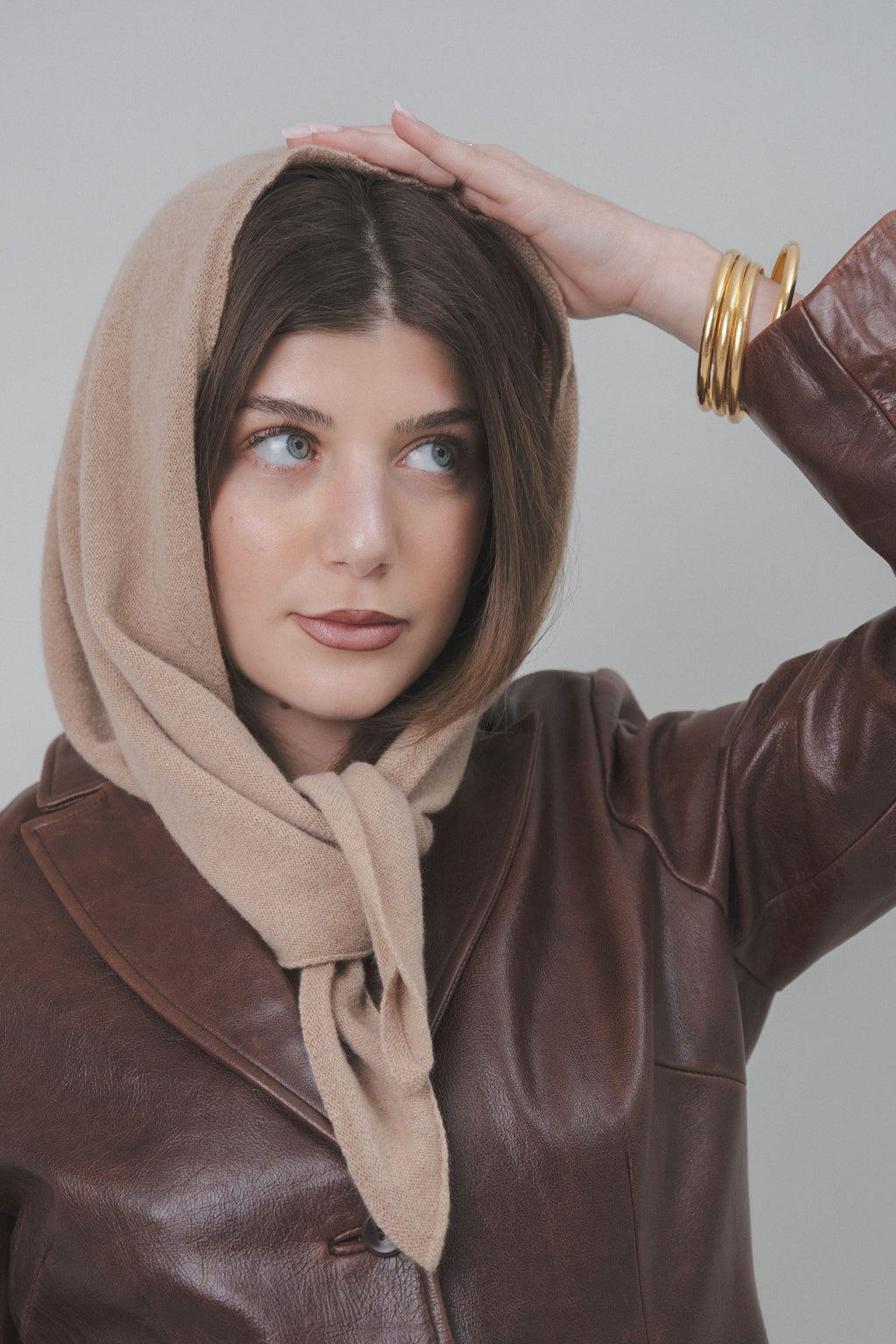 Model styling the beige Triangle Scarf by Costa Knit Atelier as a headscarf, a versatile luxury essential with a contemporary twist.