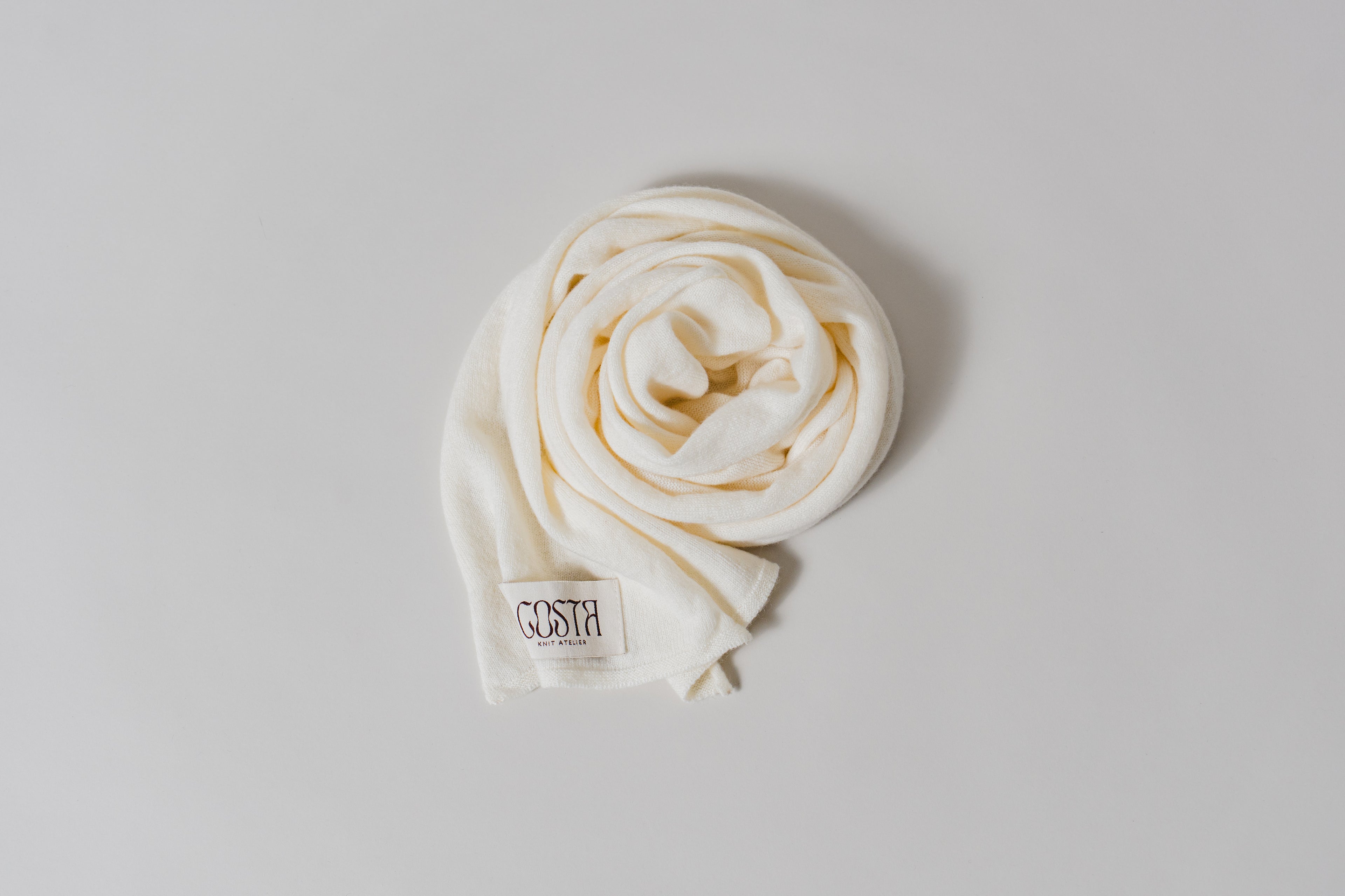 Close-up of the Costa Knit Atelier label on a luxury cashmere thin scarf in white, highlighting our use of extra-fine natural fibers and artisanal craft.