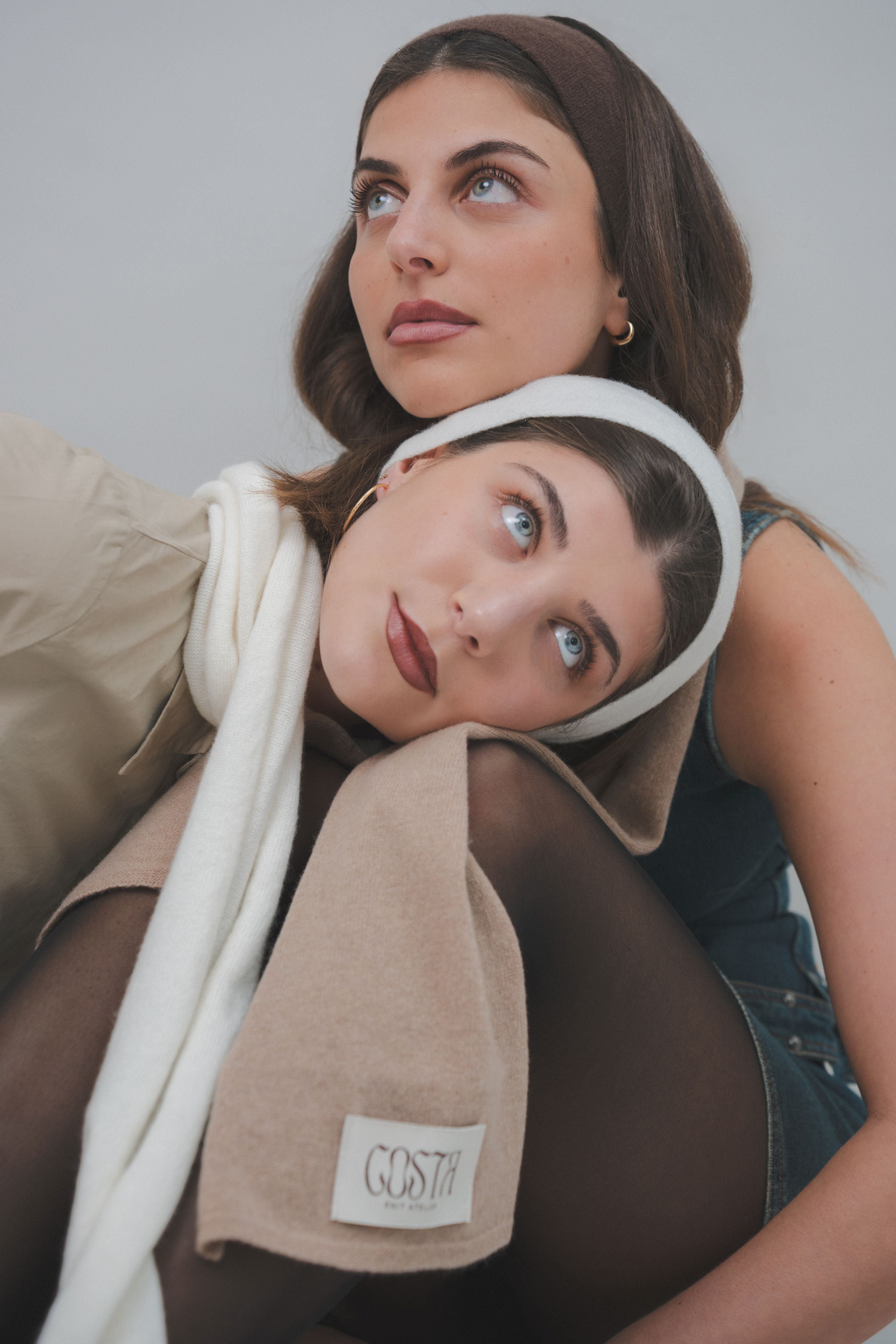 Artistic editorial shot of a model with a beige scarf and raw wool yarn balls, highlighting Costa Knit Atelier's artisanal hand-knitting heritage